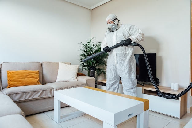 Man wearing PPE disinfecting the living room of a house with a COVID-19 disinfectant machine. Pandemic healthcare concept