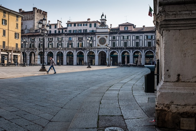 Photo a man wearing a protective face mask carries a shopping bag and crosses an empty square.