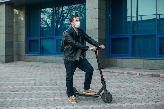 Человек, носящий защитную маску на улице, используя электрический скутер