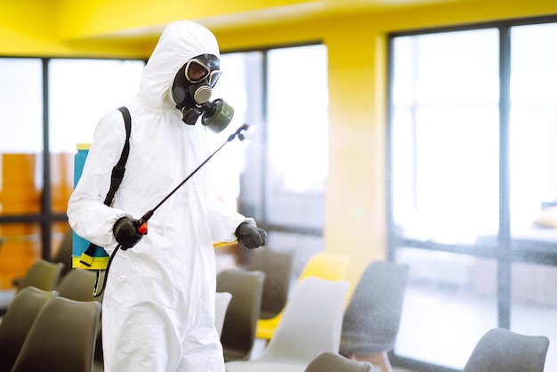 Man wearing protective suit disinfecting assembly with spray chemicals to preventing coronavirus