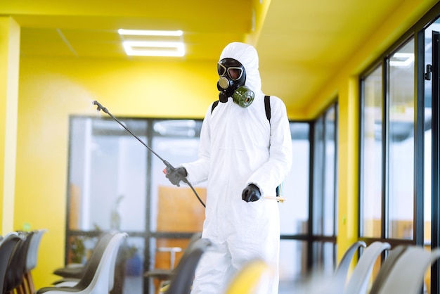 Man wearing protective suit disinfecting assembly with spray chemicals to preventing coronavirus