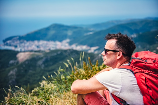 Man wearing red backpack sitting on the ground 