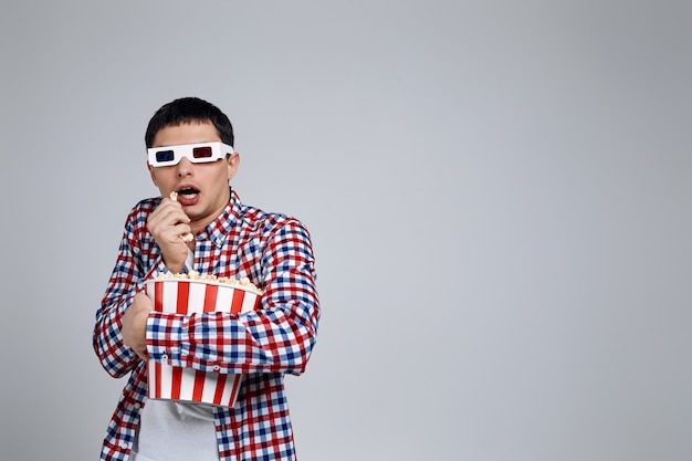 man wearing red-blue 3d glasses and eating popcorn from bucket while watching a horror movie isolated on gray