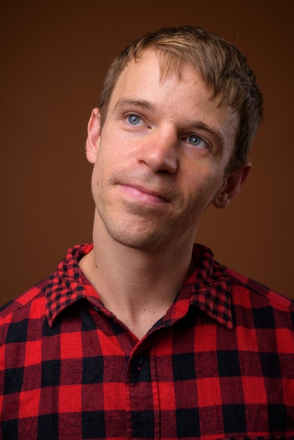 man wearing red checkered shirt against brown wall