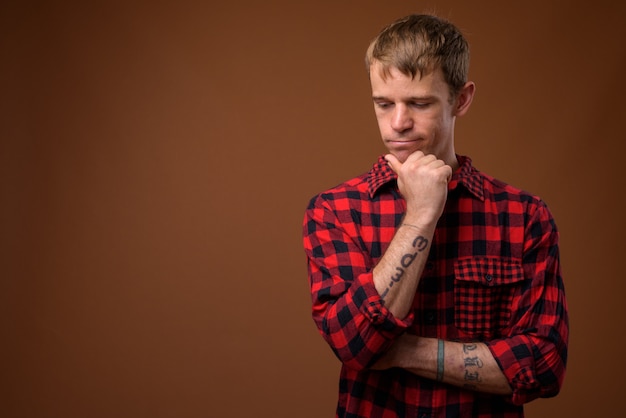 man wearing red checkered shirt against brown wall