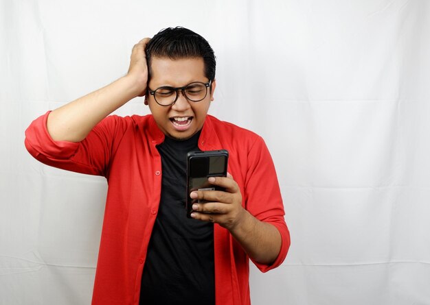 Photo a man wearing a red jacket is holding a phone with his hand on his head.