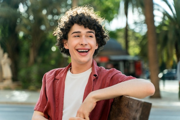 Man wearing red shirt sitting at the bench and laughing out loud while walking