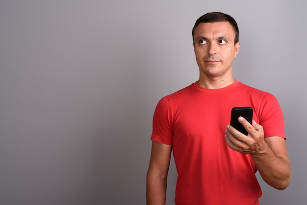 Equipaggi la camicia rossa d'uso mentre usando il telefono cellulare contro la parete grigia