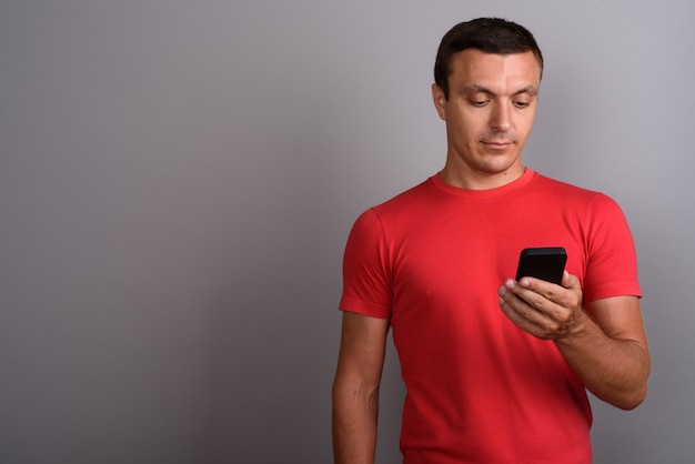 Man wearing red shirt while using mobile phone against gray wall