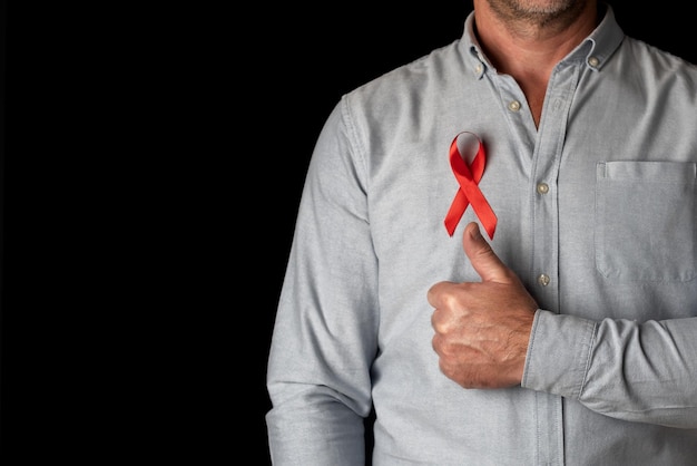 A man wearing a red World AIDS Day ribbon with his thumb up in support of all HIV positive people