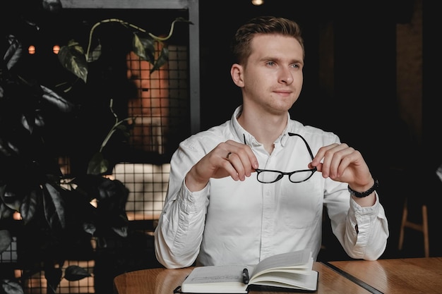 Man wearing sitting at  table holding pen takes notes to his agenda on a dark background in office