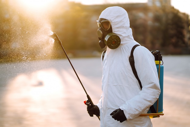 A man wearing special protective disinfection suit sprays sterilizer in the empty public place at dawn in the city of quarantine. Covid -19. Cleaning concept.