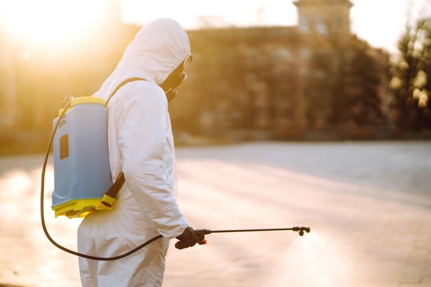 Foto un uomo che indossa una tuta disinfettante protettiva speciale spruzza lo sterilizzatore nel luogo pubblico covid 19