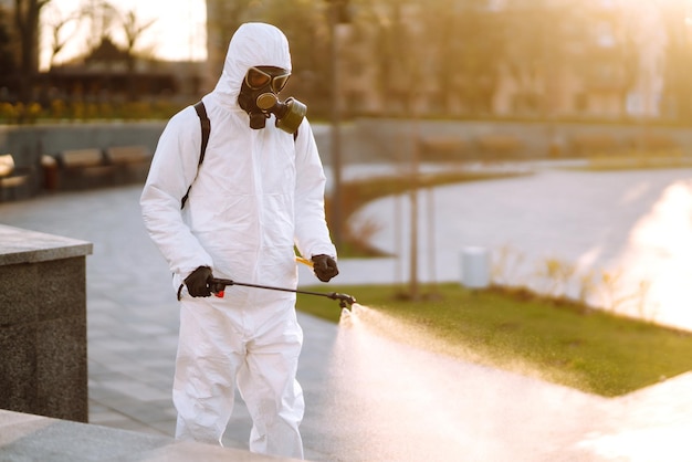 A man wearing special protective disinfection suit sprays\
sterilizer in the public place covid 19