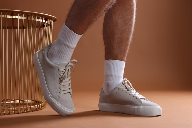 Man wearing stylish sneakers on brown background closeup