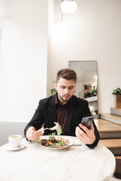 スーツとひげを着た男性が居心地の良いレストランでスマートフォンを使用しています。