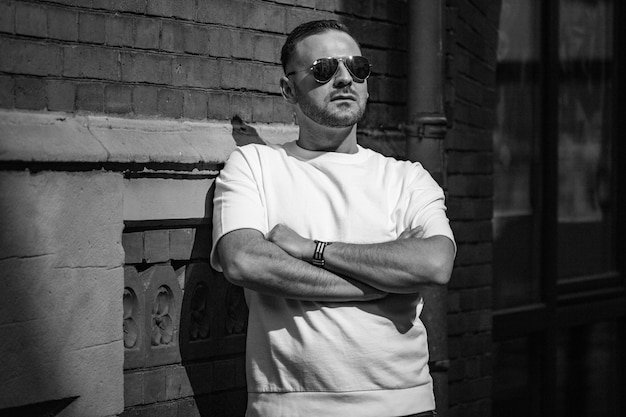 Photo man wearing sunglasses while standing by brick wall on sunny day