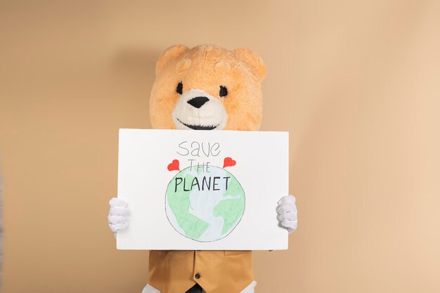 Man wearing a teddy bear mask on a yellow background holding a cardboard sign that says 39Save the planet39 Concept of caring for the planet and global warming