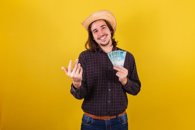 Man wearing typical clothes for party Junina Calling with hands inviting holding money