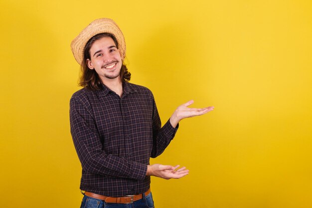 Man wearing typical clothes for party Junina presenting with hands space for advertising and text