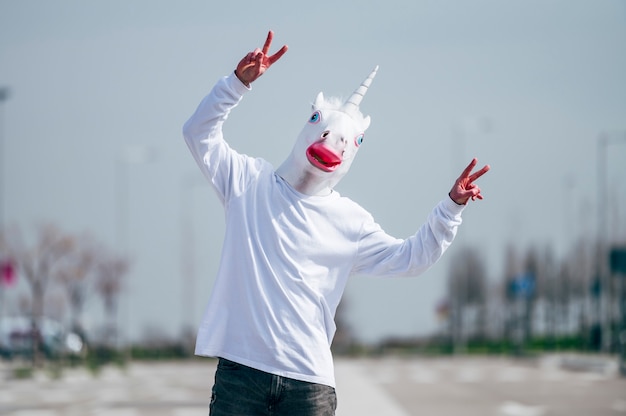 Man wearing unicorn mask making victory gesture with fingers