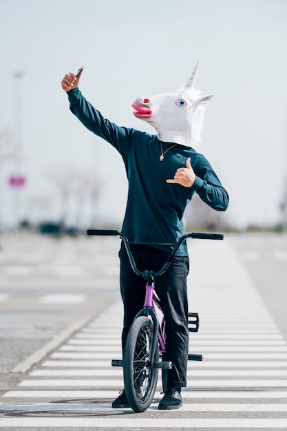 Foto uomo che indossa la maschera di unicorno di scattare una foto con lo smartphone