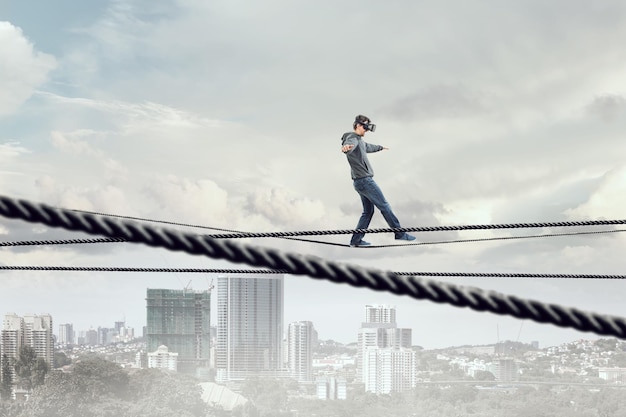 Man wearing virtual reality goggles and balancing on rope. Mixed media