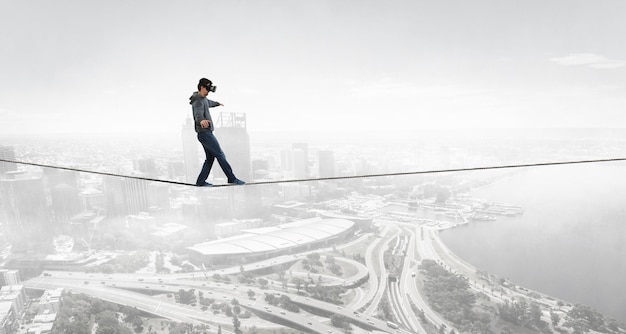 Man wearing virtual reality goggles and balancing on rope. Mixed media