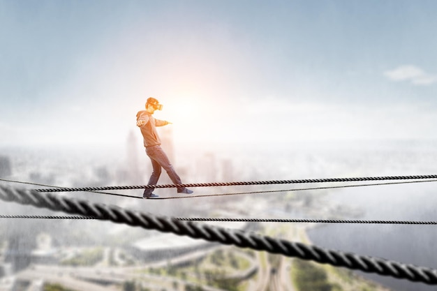 Man wearing virtual reality goggles and balancing on rope. Mixed media