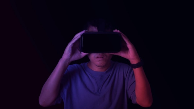 ネオンカラーの背景にバーチャルリアリティヘッドセットを身に着けている男VR未来技術オンラインコンセプトバーチャルリアリティのメガネとメタバーステクノロジーゲームエンターテインメントコンセプトを探る