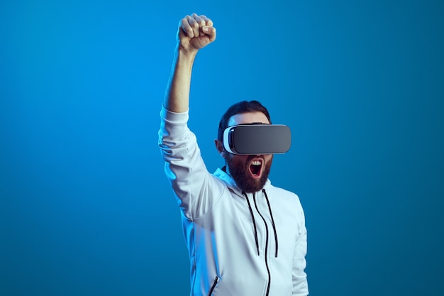 Man wearing vr headset on standing with raised hand and screaming over blue