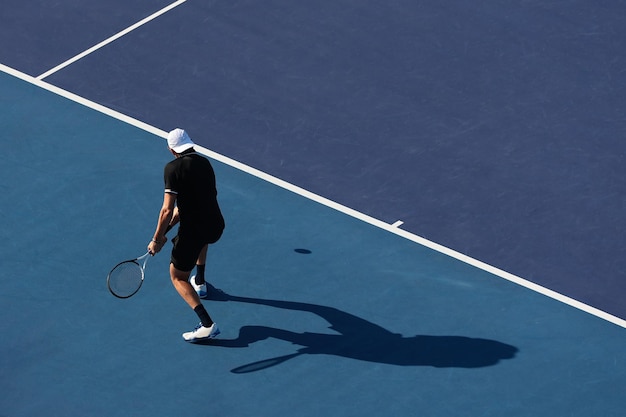 흰 모자를 쓴 남자가 파란 테니스 코트에서 테니스를 치고 있다