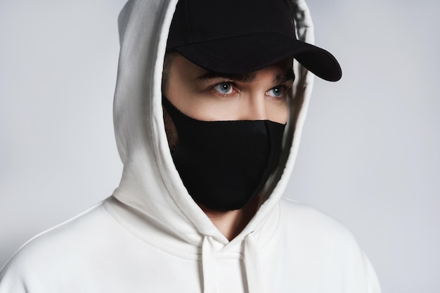 Man wearing white hoodie black baseball cap and cloth face mask