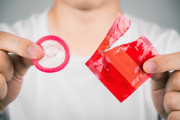 Photo man wearing white t-shirt and hand tearing a red condom.