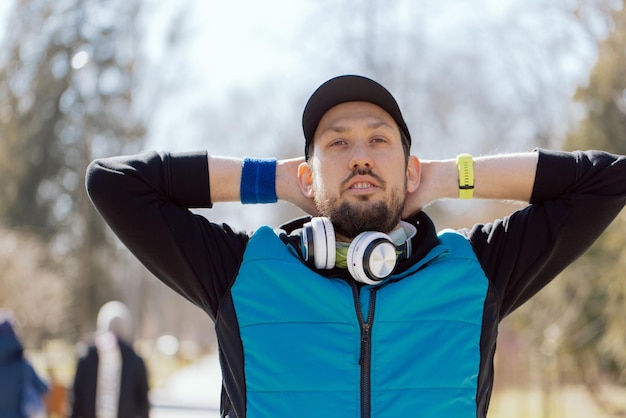 Man wearing wireless headphones jogging in the park in warm\
clothes outdoor leisure exercise running