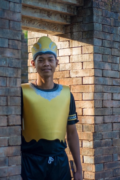 Photo a man wearing a yellow crown stands in front of a brick wall.