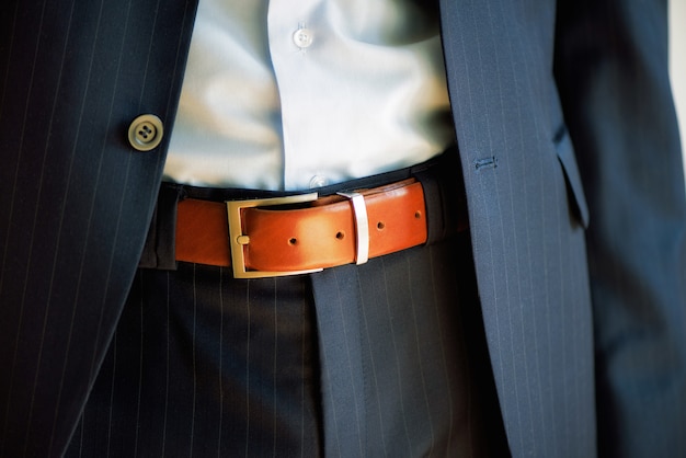 Man wears belt. Young businessman in casual suit with accessories. Fashion and clothing concept. Groom getting ready in morning before ceremony