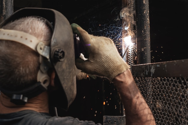 Photo man in welder mask and gloves is engaged in welding metal structure