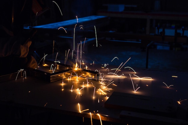 A man welder with construction gloves and a welding mask is welded with a welding machine metal in workshop