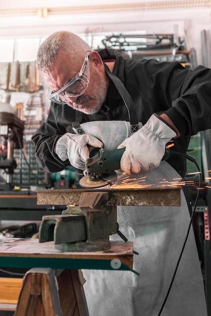 A man welder with safety glasses polishes the metal angle grinder in a workshop