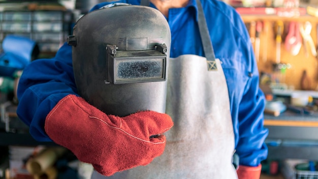 Un uomo saldatore con casco di sicurezza che lavora con saldatrice ad arco in officina