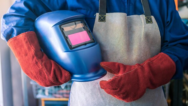 Un uomo saldatore con casco di sicurezza che lavora con saldatrice ad arco in officina