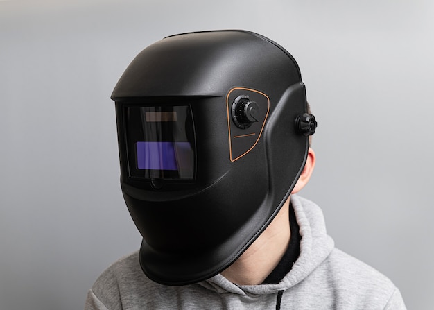 Man in a welding black mask on a light gray wall, close-up