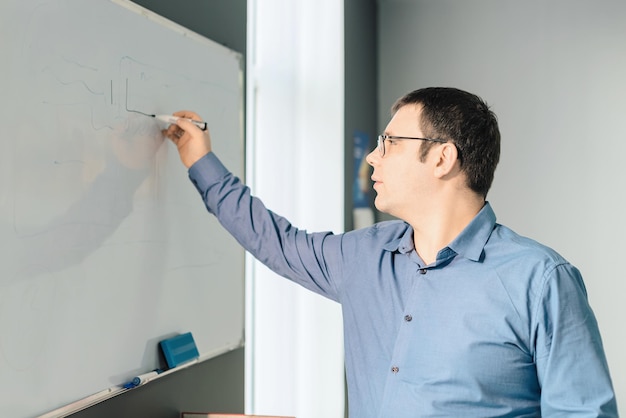 Man werknemer in blauw shirt en bril schrijven iets op wit bord tijdens zakelijke bijeenkomst op kantoor Zakelijke drukke werkdag concept