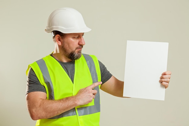 Man werknemer in een vest en een witte bouwhelm hoed met een wit laken in zijn handen op een wit