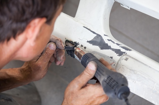 Man werknemer met industrieel soldeerpistool van zwarte kleur op de vloer tussen stof en gereedschap voor het verwarmen en smelten van plastic tijdens het aansluiten van onderdelen in de werkplaats voor reparatie van autobumpers