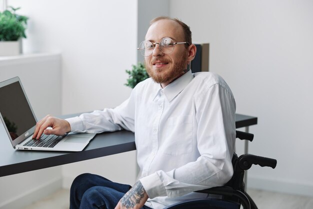 Foto un uomo d'affari in sedia a rotelle in ufficio che lavora al computer portatile lavorando online social network avvio integrazione nella società il concetto di lavorare una persona con disabilità una persona reale primo piano