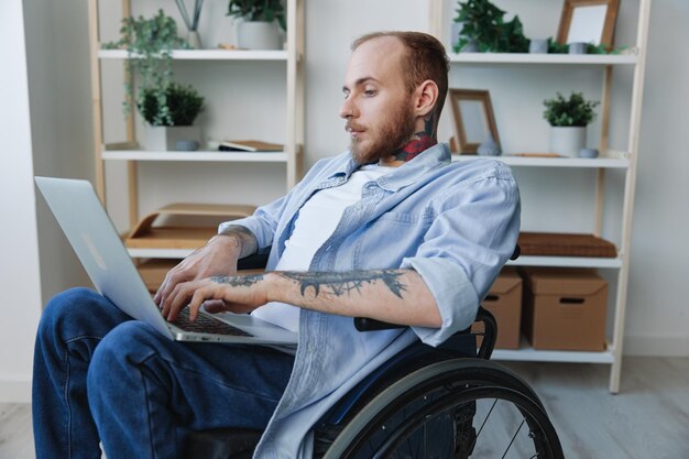 A man in a wheelchair freelancer works at a laptop at home work online social networks and startup copy space integration into society concept of health disabled person real person closeup