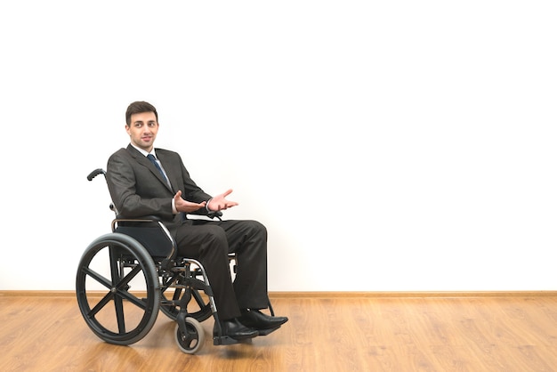 The man in the wheelchair gesturing on the white wall background