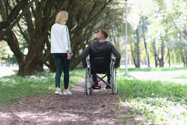 휠체어를 탄 남자가 여자친구와 함께 공원을 걷고 있다.